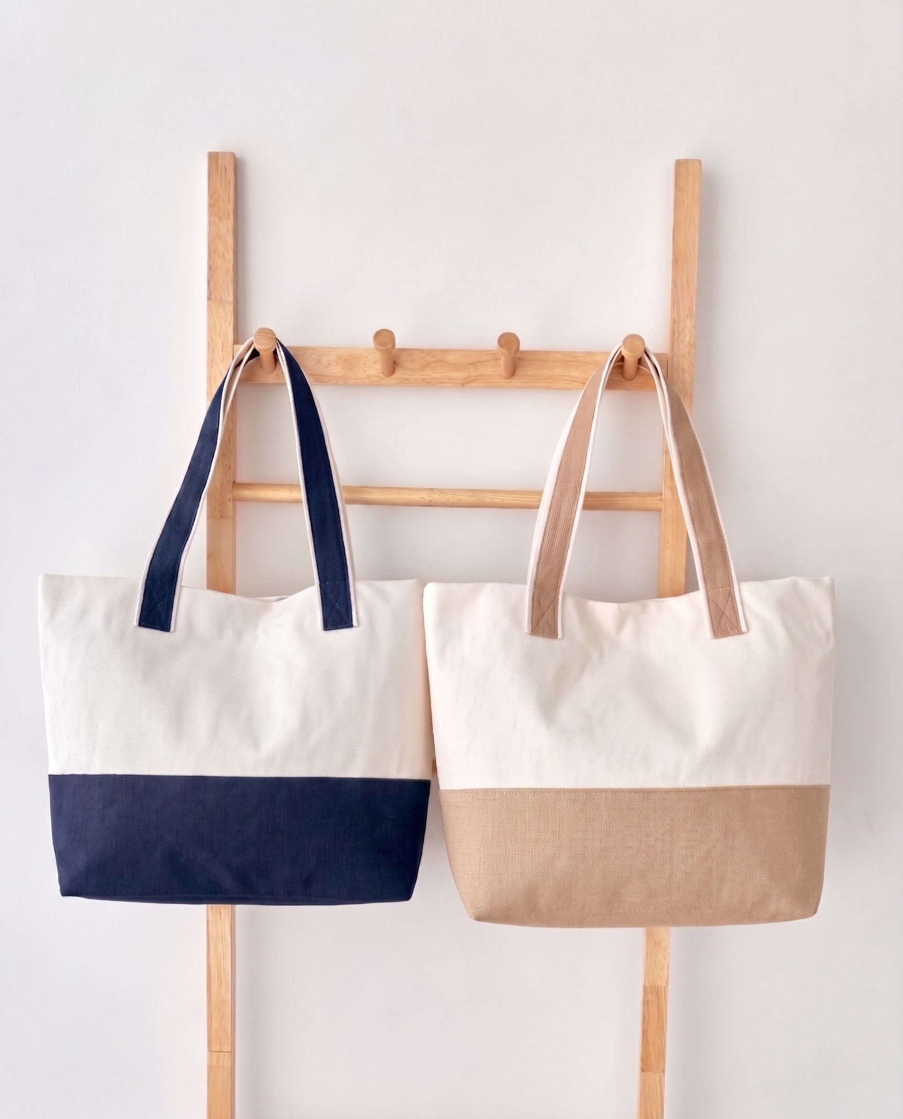 Two canvas totes hanging on a wooden rack, navy and beige colourways, both shown blank without embroidery