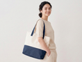 Load image into Gallery viewer, Woman holding a white tote bag with navy accents against a plain background
