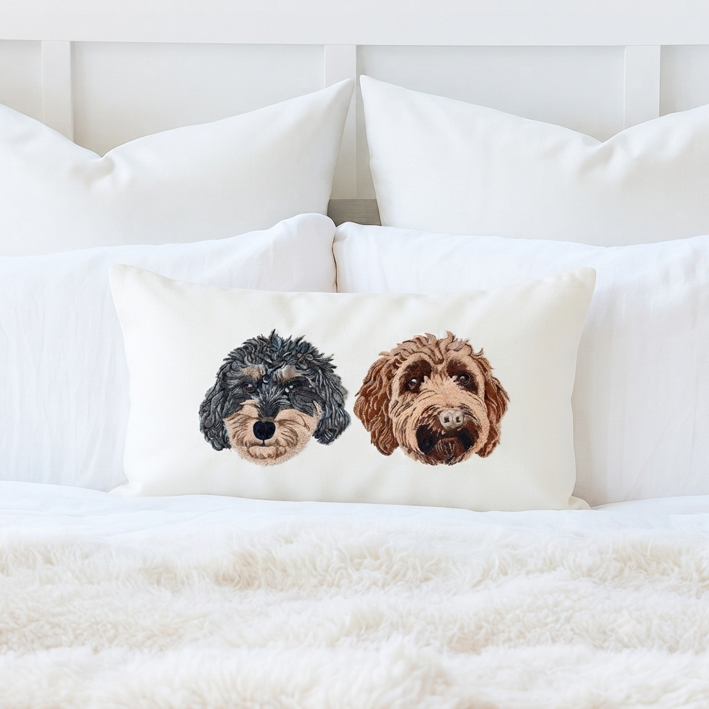 Cream 12 by 20 lumbar pillow cover on a white bed, embroidered with two doodle portraits, one black and one apricot
